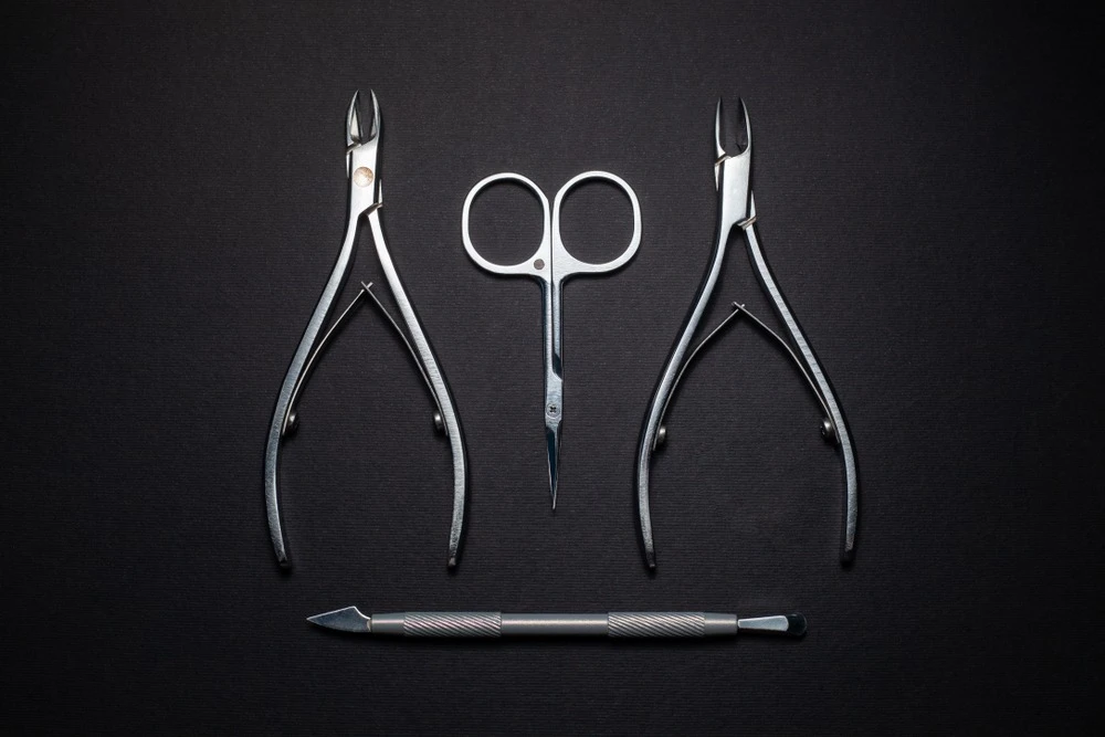 Manicure tools: cuticle nippers, scissors, and nail file, symmetrically arranged on a dark surface