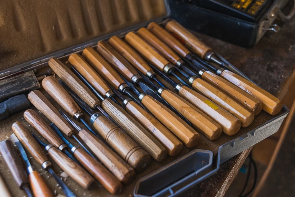 A set of wood-handled chisels in various sizes, neatly arranged in a toolbox.